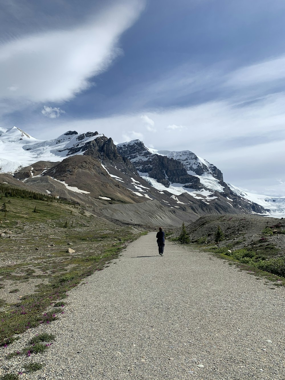 person walking on gray asphalt road near snow covered mountain during daytime