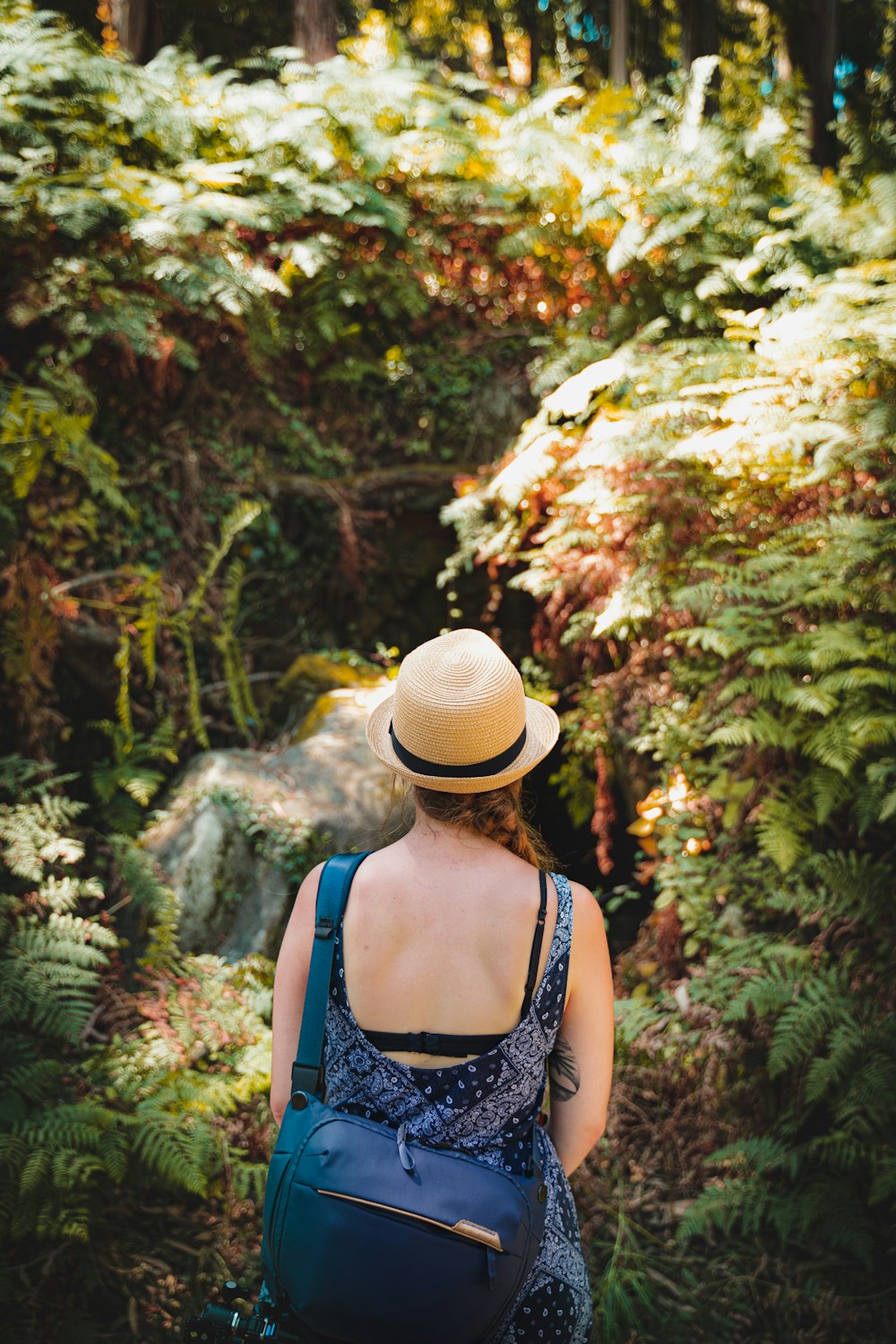 woman in black and white floral tank top and brown hat standing near green trees during