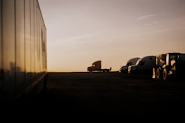 A fleet of trucks parked in front of a logistics warehouse at sunset.