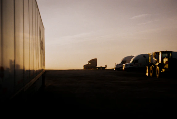 A friendly dispatcher speaking on a headset with trucks moving in the background at sunset.