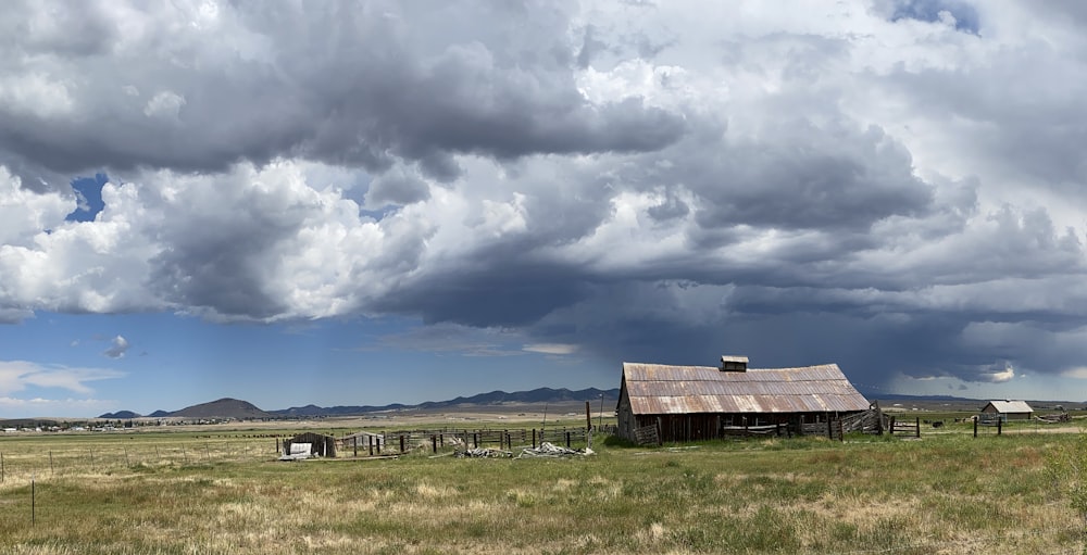 brown wooden house on green grass field under white clouds and blue sky during daytime