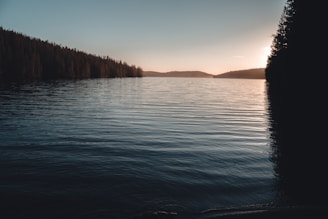 A serene lake view at sunset with mountains in the background, reflecting calm waters.
