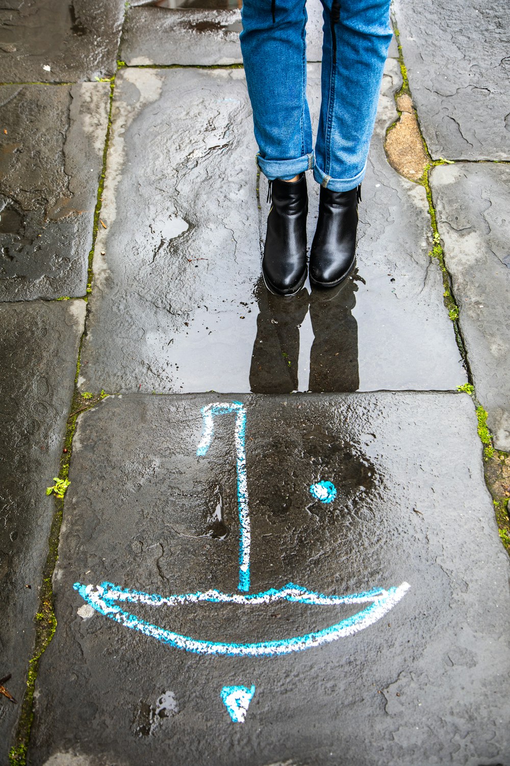 Persona in jeans blu denim e stivali neri in piedi sul pavimento di cemento grigio