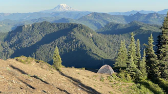 A tent pitched on a grassy mountain slope under a clear blue sky.