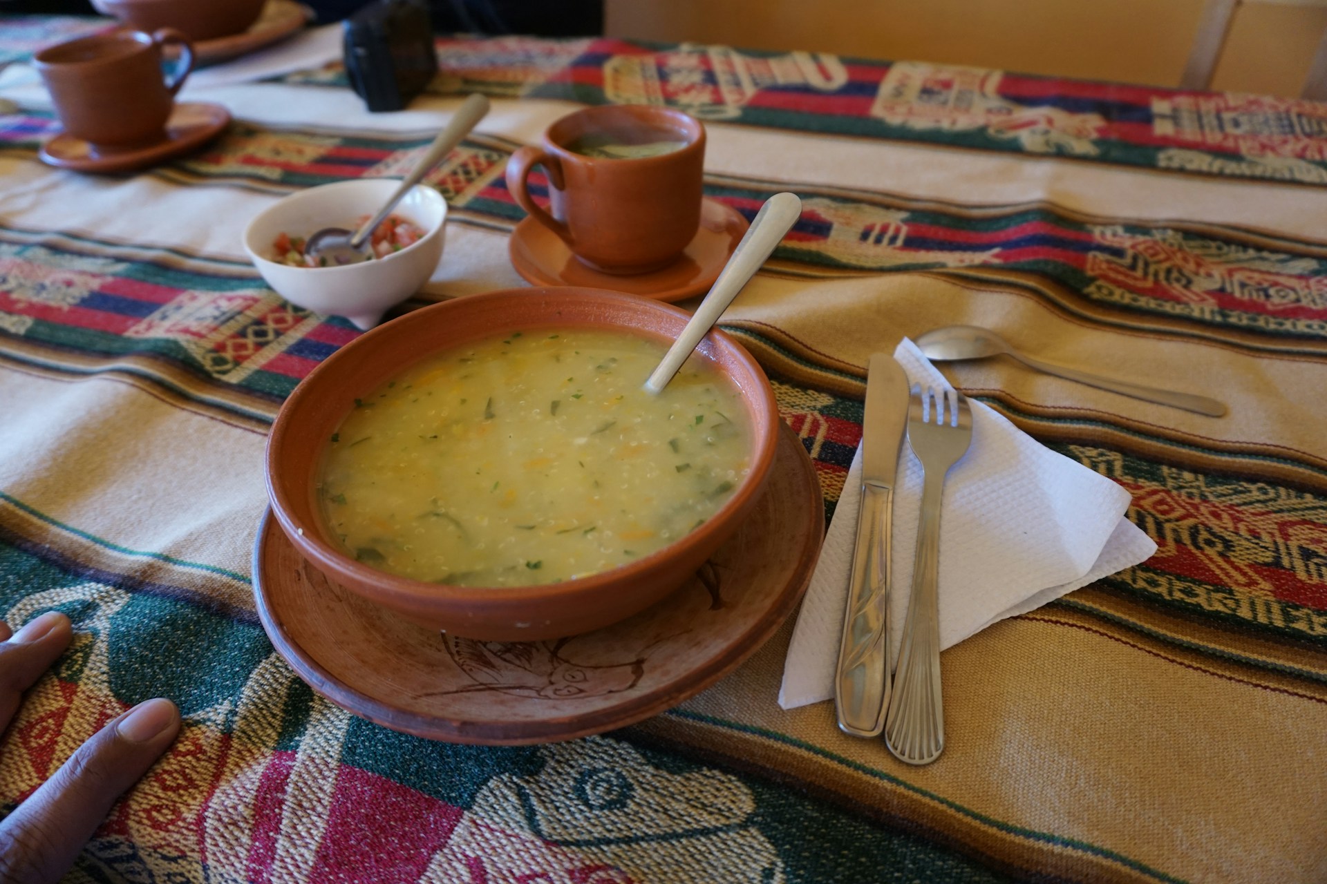 A rustic wooden table set with a steaming bowl of mute santandereano, surrounded by fresh corn and local herbs.