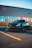 A sleek black sports car is parked in front of a commercial building with a sign for 'east end DENTAL.' The car has a glossy finish and is positioned on an asphalt parking lot, marked with yellow lines. The building has large windows reflecting the surrounding area.