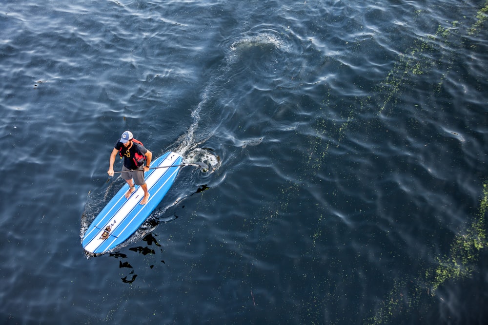 man in black shorts riding blue and white kayak on body of water during daytime