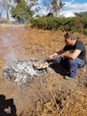 A hiker cooking a meal on a SteelTrail Grill atop a rocky outcrop with panoramic views.