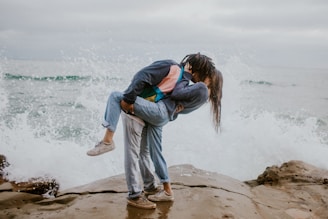 woman in blue jacket and gray pants carrying woman in blue jacket on beach during daytime
