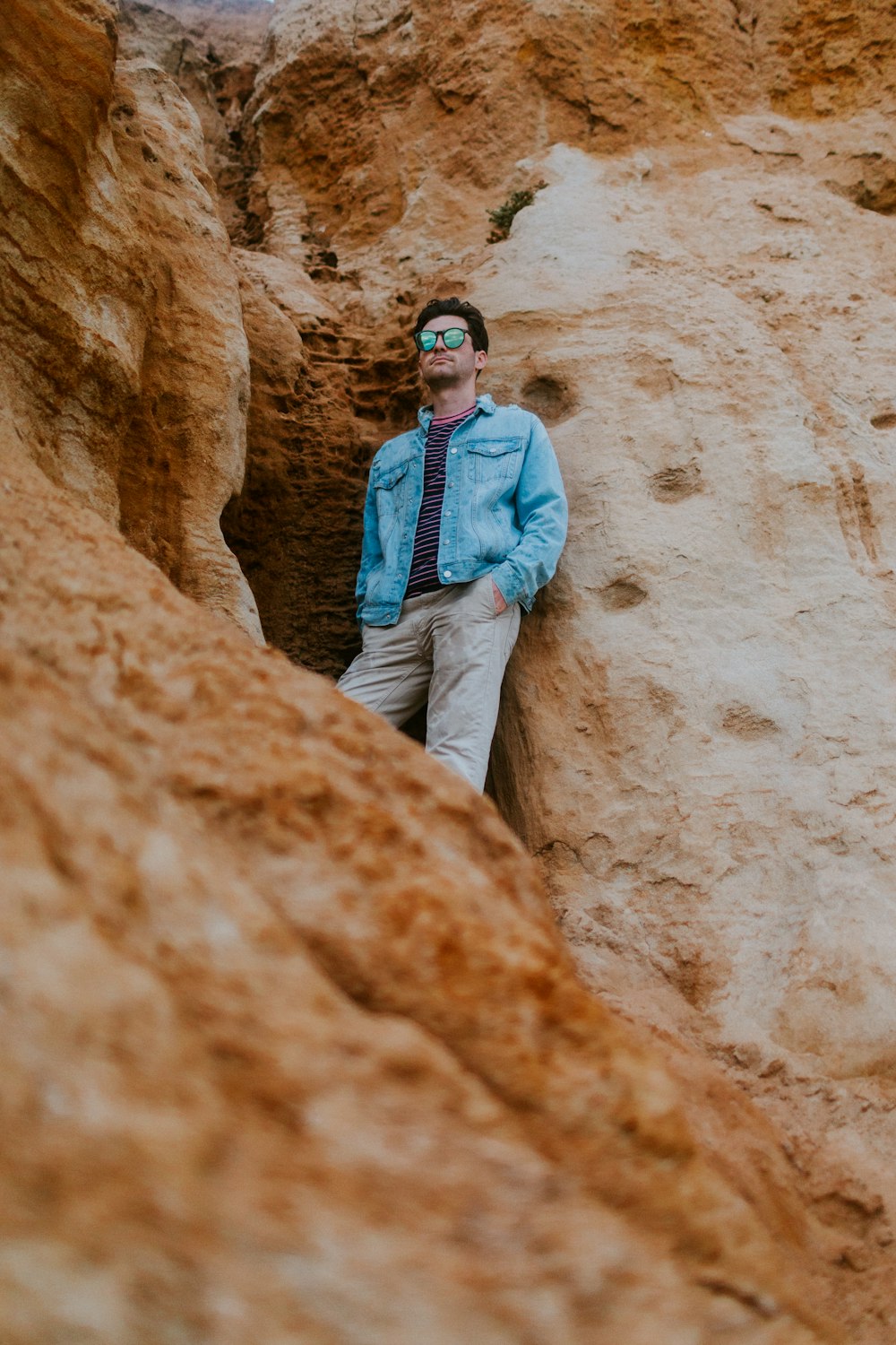 man in blue denim jacket and brown pants standing on brown rock formation during daytime