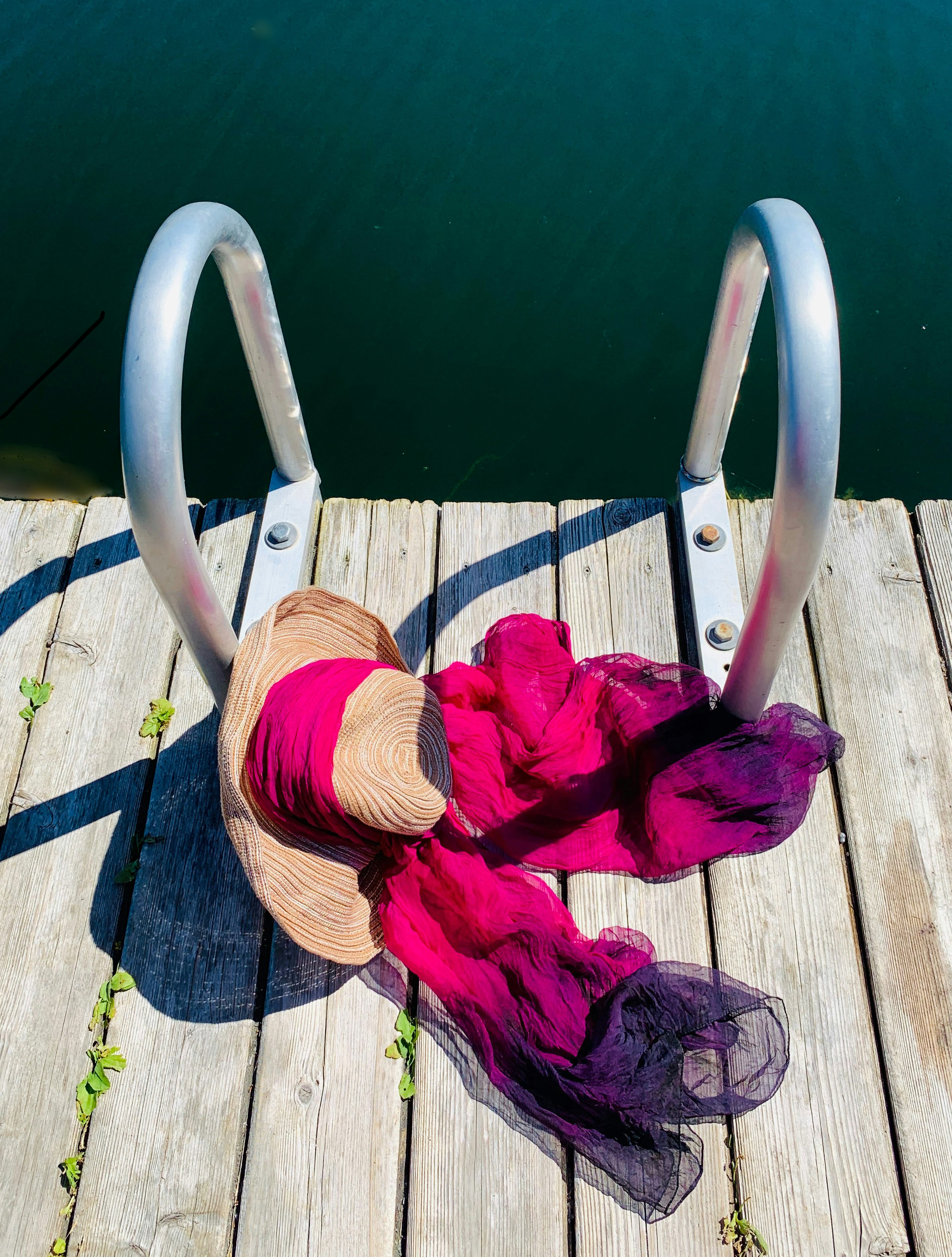 Magenta scarf around straw hat on dock next to dark green water on a private lake near Kettle Falls, Washington (high desert country)