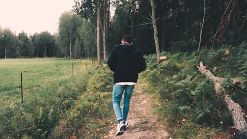 woman in black jacket and blue denim jeans walking on green grass field during daytime