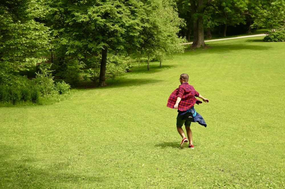 昼間、緑の芝生の上を走る赤いシャツの少年