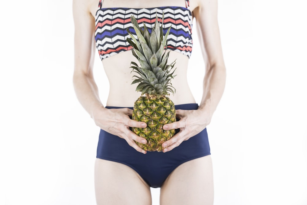 woman in blue and green floral bikini holding pineapple fruit
