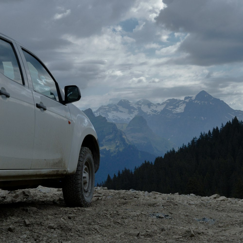 white suv on rocky ground near green trees and snow covered mountains during daytime