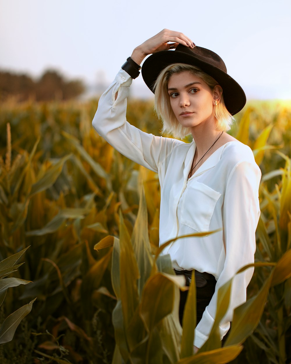 woman in white long sleeve shirt wearing black hat standing on corn field during daytime