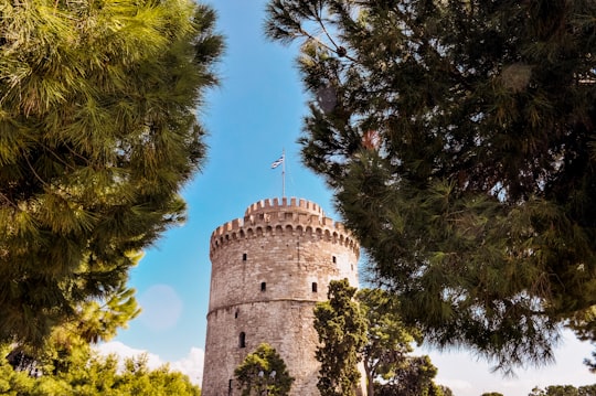 brown concrete castle surrounded by green trees under blue sky during daytime in White Tower of Thessaloniki Greece