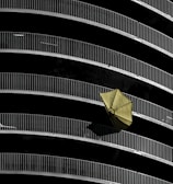 Curved balconies with metal railings create a repetitive pattern against a dark background. A single yellow umbrella is prominently displayed hanging off one of the railings, adding contrast to the composition.