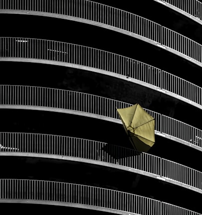 Curved balconies with metal railings create a repetitive pattern against a dark background. A single yellow umbrella is prominently displayed hanging off one of the railings, adding contrast to the composition.