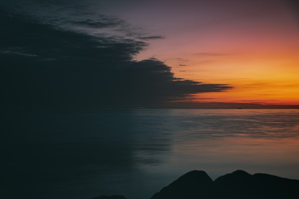 silhouette of mountain near body of water during sunset