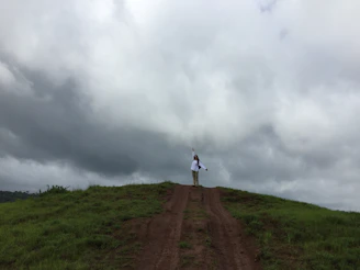 Illustration of the Page of Swords standing on a windy hilltop, sword raised high against a cloudy sky