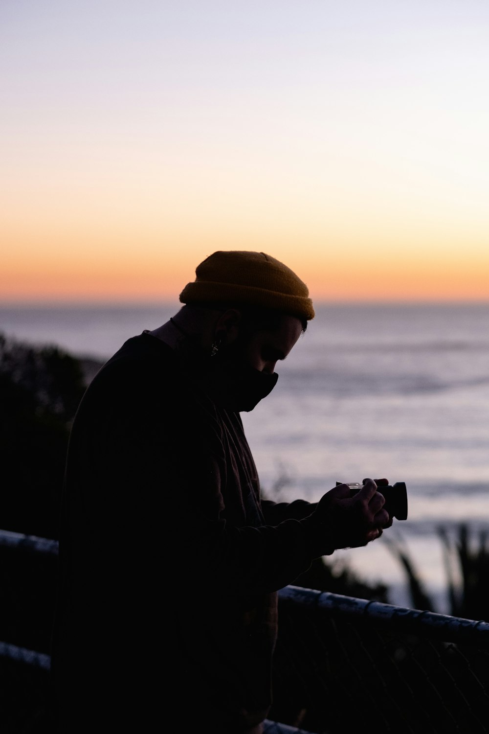 man in black jacket and brown hat holding camera during sunset