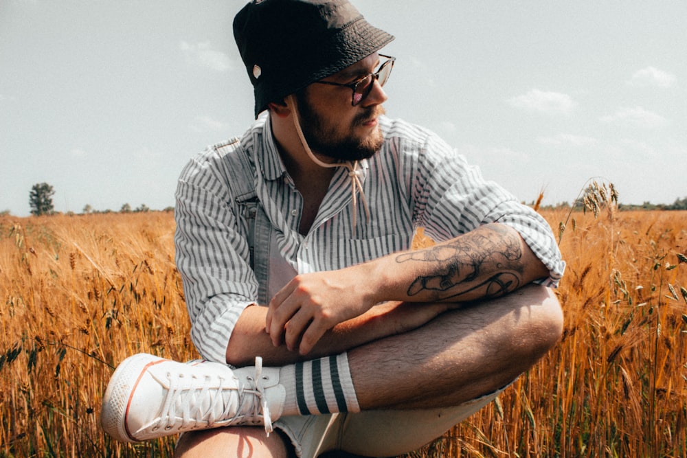 man in white and black stripe button up shirt and black cap sitting on brown grass
