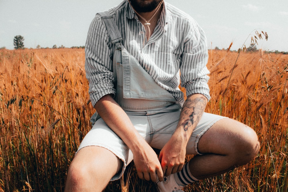 man in white and black stripe button up shirt sitting on brown grass field during daytime