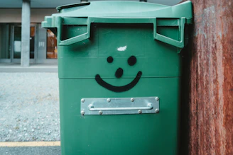A friendly CD Property Care team member in uniform smiling while holding a bright green trash bin outside a clean suburban home.