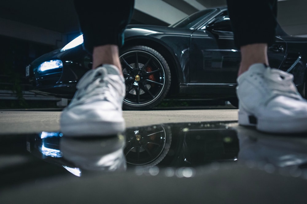 person in black pants and white shoes standing beside black car