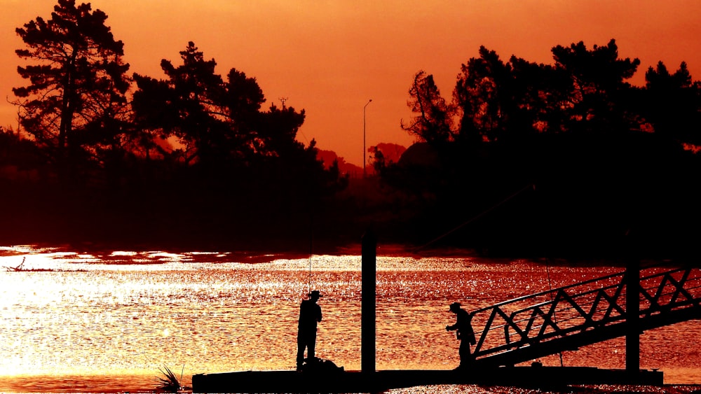 silhouette di persona in piedi sul molo durante il tramonto