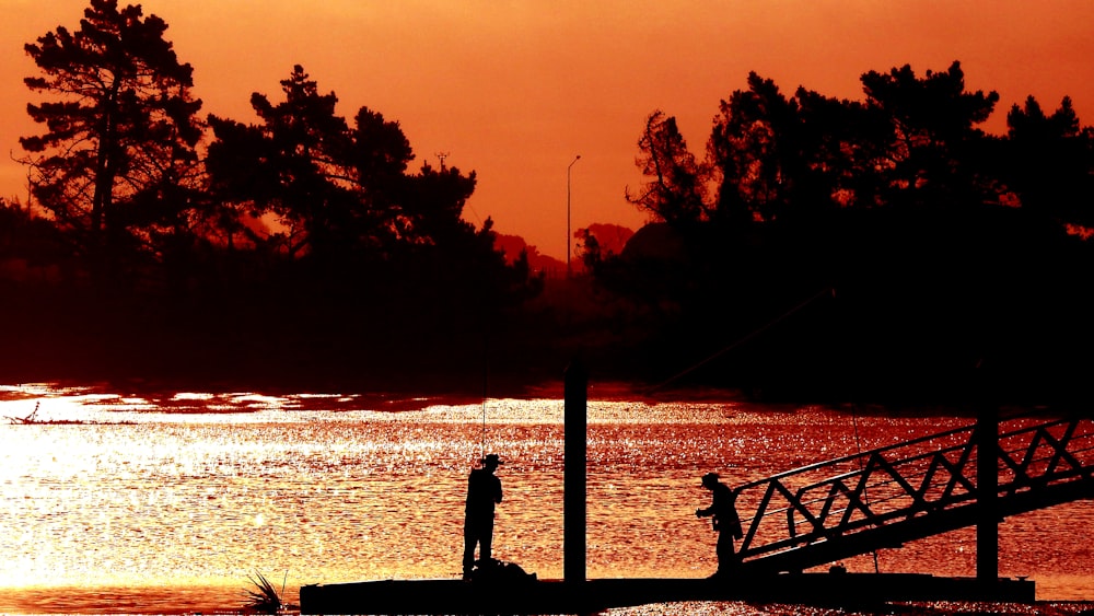 silhouette of person standing on dock during sunset