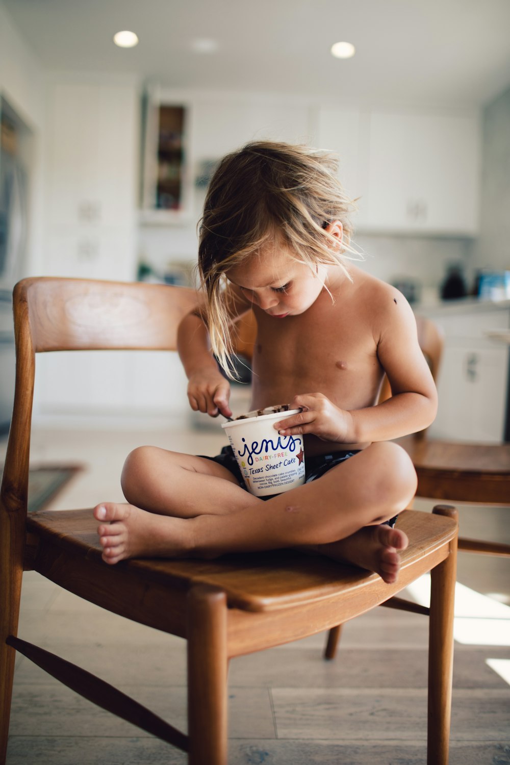 topless girl sitting on brown wooden chair holding white and blue labeled can