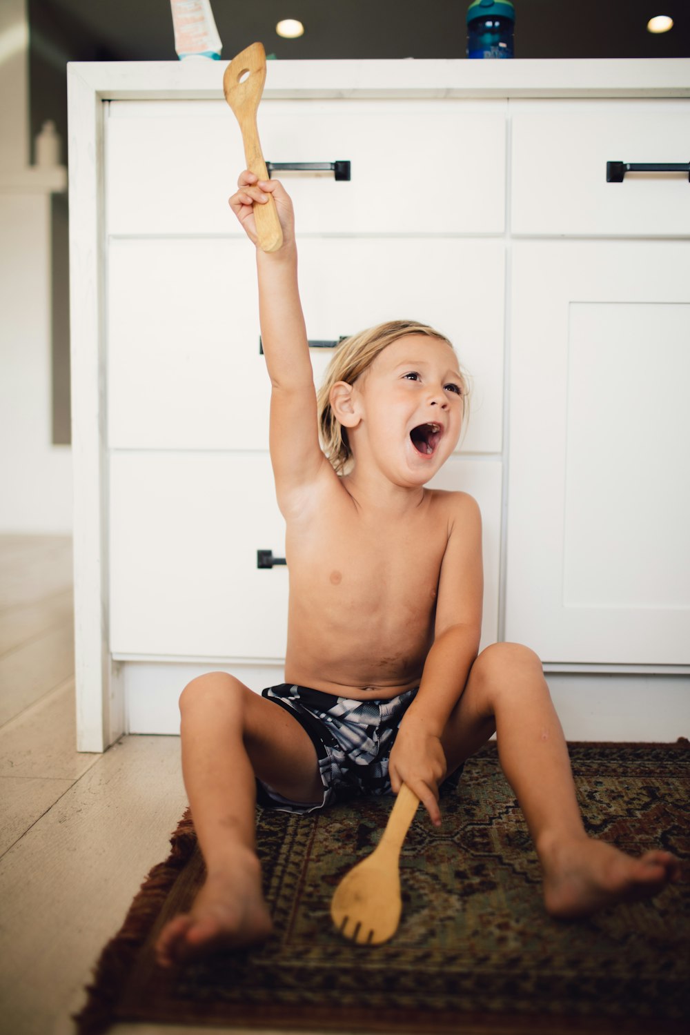 topless boy in blue shorts sitting on floor