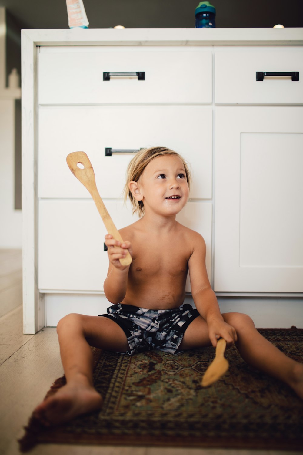 topless boy in blue and white shorts sitting on floor