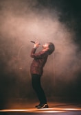 A vocalist passionately singing into a microphone with a smoky venue backdrop.