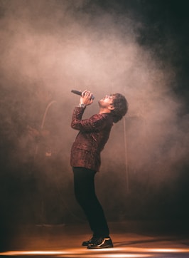 man in brown and black plaid dress shirt singing on stage