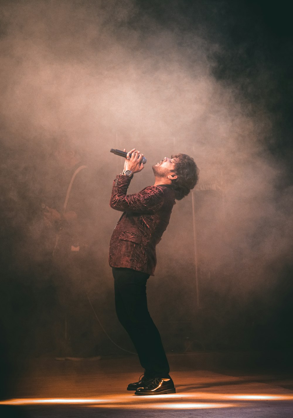 man in brown and black plaid dress shirt singing on stage