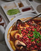 A steaming bowl of asam pedas ikan pari with fresh herbs on a cream-colored ceramic bowl.