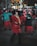 A group of people are participating in an outdoor group dance session, wearing colorful and warm clothing appropriate for a cool evening. The setting appears lively and social, with everyone seeming to enjoy themselves, suggesting a community or recreational event.