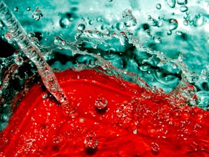 A dynamic splash of liquid combining vibrant red and teal hues, with bubbles and droplets captured in motion, creating an abstract, fluid scene.