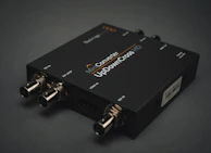 A black electronic device with various input and output ports labeled SDI IN, SDI LOOP, HDMI IN, and USB. The label on the device reads 'Mini Converter UpDownCross HD'. It is placed on a dark surface, and the connectors are visible in a metallic finish.