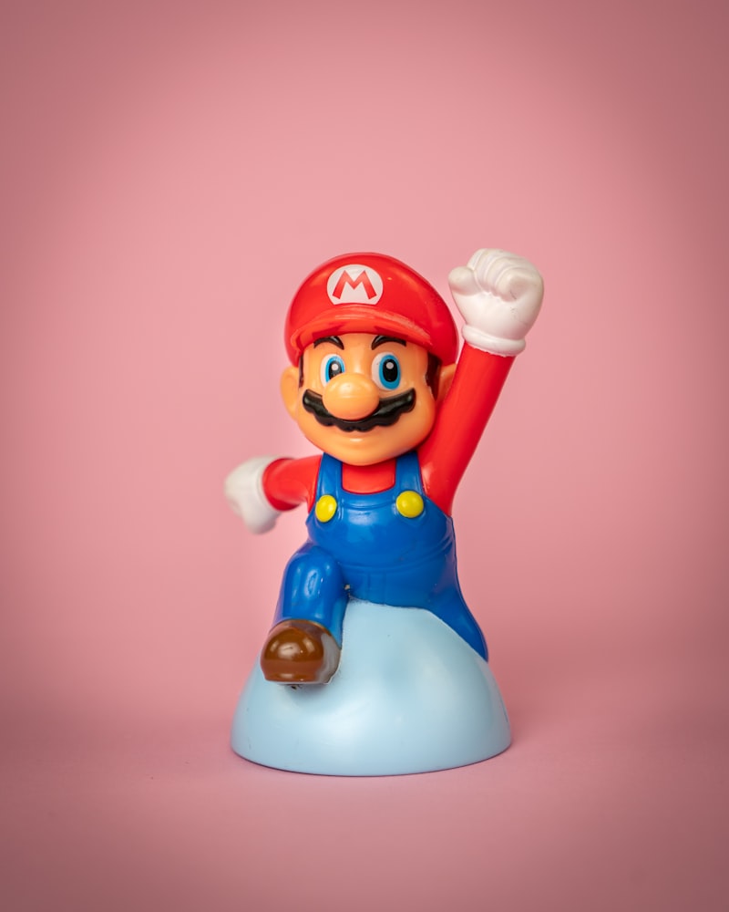 A Mario figurine pumping his fist in front of a pink background