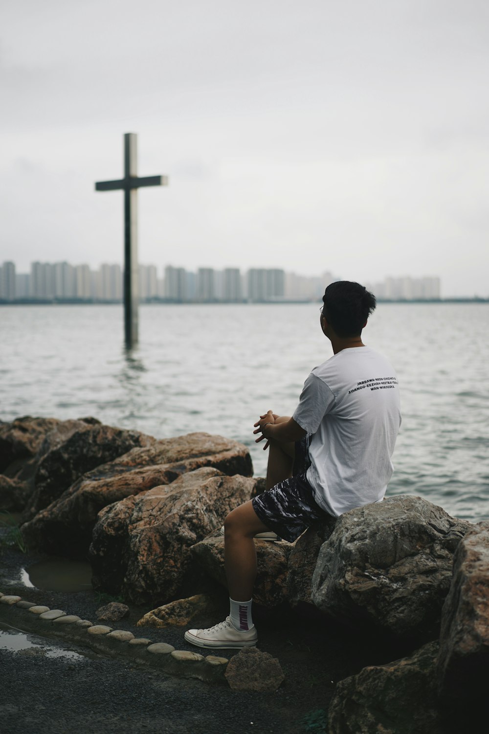 man in white shirt sitting on brown rock near body of water during daytime