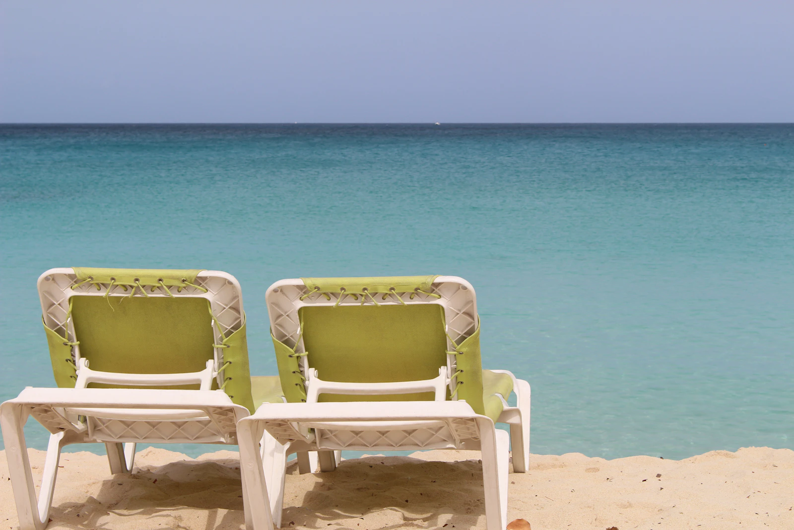 Simple beach chairs on pale sand facing calm turquoise Caribbean water — the kind of affordable shoreline these resorts sit on