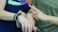 Two individuals are shown interacting with their smartwatches, wearing casual clothes with bright, colorful nail polish on neatly manicured hands. The person on the right is pointing towards the watch on the left wrist, and there are additional accessories like bracelets visible.