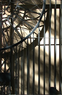 Intricate metalwork casts complex geometric shadows on a sunlit beige wall, creating an interplay of light and shadow with diagonal and circular patterns.