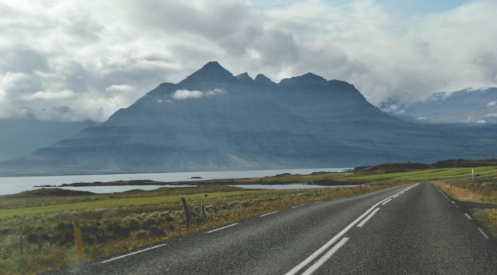 gray concrete road near mountain under white clouds during daytime