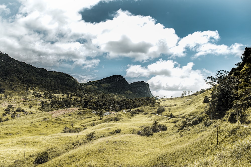 green grass field and mountains under white clouds and blue sky during daytime