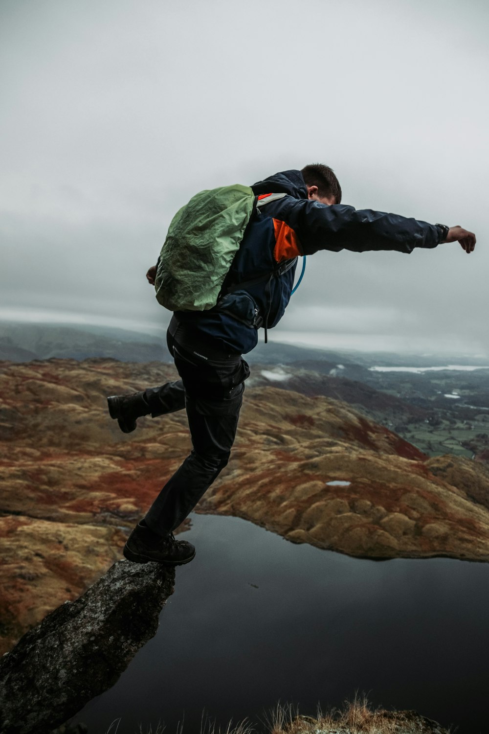 man in green jacket and black pants standing on rock formation during daytime